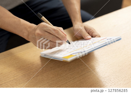 Male hand holding pen marking on calendar page on desk table. 127856285