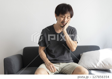 Mature Asian man suffer from toothache with painful expression, sitting on sofa at home. Mature Asian man suffer from toothache with painful expression, sitting on sofa at home. 127856354
