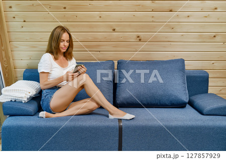 Woman in a T-shirt and shorts sitting on the sofa with a smartphone in her hands 127857929