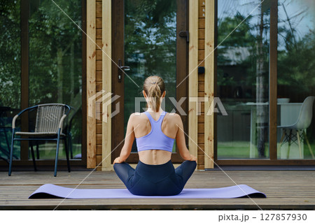 Back view of a woman sits on a yoga mat placed on a wooden terrace of tiny house 127857930