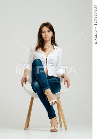 Teenager sitting elegantly in a chair wearing stylish outfit and casual shoes 127857937