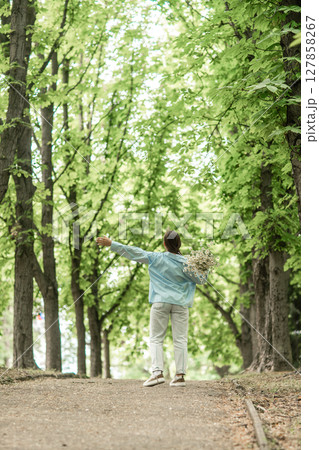 Woman Flowers Park: Back view, girl holds daisies, walks in summer park enjoying nature, daytime. Woman Flowers Park: Back view, girl holds daisies, walks in summer park enjoying nature, daytime. 127858267