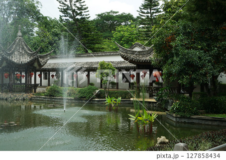 Traditional Chinese garden with a pond and a pavilion adorned with red lanterns 127858434