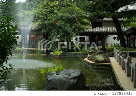 Traditional Chinese garden with a pond and a pavilion adorned with red lanterns 127858435