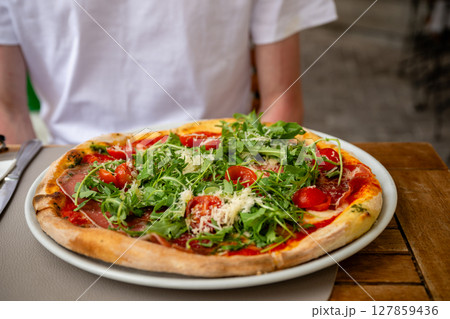 Fresh Italian pizza with arugula, cherry tomatoes, prosciutto and parmesan served at outdoor cafe 127859436
