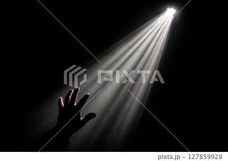 A Hand Reaching Toward a Distant Light in the Darkness Symbolizing Hope and Spiritual Connection 127859928