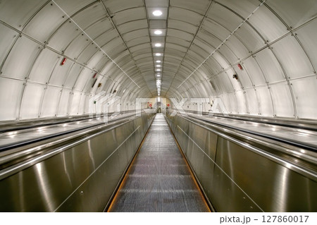 A long, narrow, silver and gray tunnel with a silver escalator A long, narrow, silver and gray tunnel with a silver escalator 127860017