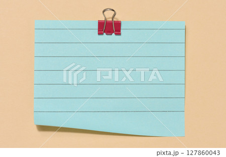 Blue sticky note secured with a red paper clip, centered on a beige background. 127860043