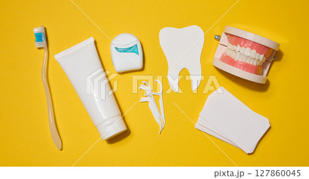 Toothbrush, white tube of toothpaste, dental floss in a case, white tooth cut out of paper, model of dentures on a bright yellow background. Toothbrush, white tube of toothpaste, dental floss in a case, white tooth cut out of paper, model of dentures on a bright yellow background. 127860045