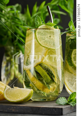Refreshing detox or summer drink in a glass with lemon, lime, mint, ice, and metal straw. Dark background 127860074