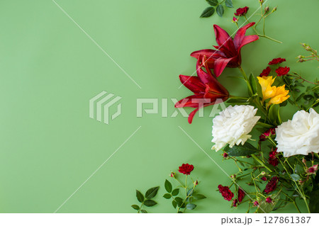 Detailed view of two large red lilies with red and white roses on a green background Detailed view of two large red lilies with red and white roses on a green background 127861387