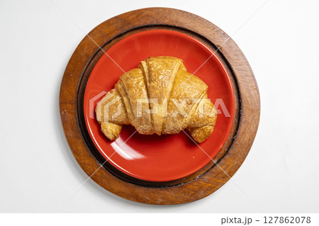 Freshly baked croissant on a red plate with a white background. Top view 127862078