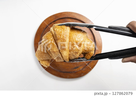 Tongs with freshly baked croissants on a wooden tray with a white background. Top view 127862079