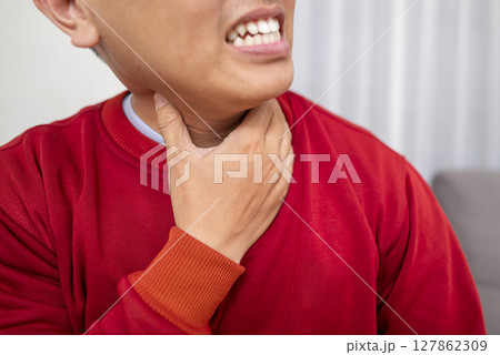 Indonesian southeast asian man sitting on the couch at home and coughing. Suffers from an attack of asthma or allergies. Healthcare concept Indonesian southeast asian man sitting on the couch at home and coughing. Suffers from an attack of asthma or allergies. Healthcare concept 127862309