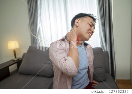 Indonesian southeast asian man suffering from neck pain while sitting on the living room couch at home. Healthcare concept 127862323