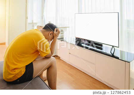 Indonesian southeast asian man watching television with depression and worry for distress and angry. Mental health and mindfulness concept. Empty television screen for mockup, template, or copy space 127862453