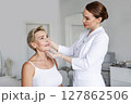Cosmetologist in white coat examining mature woman's face on professional anti-aging consultation in aesthetic clinic, checking skin before rejuvenation treatment, beauty and skincare in medical spa 127862506