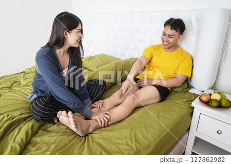 Indonesian southeast asian woman massages her husband feet in the bedroom. Self-care and wellness routines concept Indonesian southeast asian woman massages her husband feet in the bedroom. Self-care and wellness routines concept 127862982
