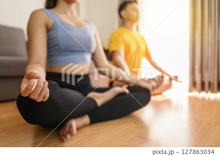 Indonesian southeast asian couple meditating in the lotus position on yoga at home for a healthy lifestyle and body care. Meditation and yoga practices concept 127863034