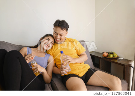 Indonesian southeast asian couple drinking water after finishing a home body workout exercise session for a fit physique and a healthy sport lifestyle at home. Fitness and active lifestyles concept Indonesian southeast asian couple drinking water after finishing a home body workout exercise session for a fit physique and a healthy sport lifestyle at home. Fitness and active lifestyles concept 127863041