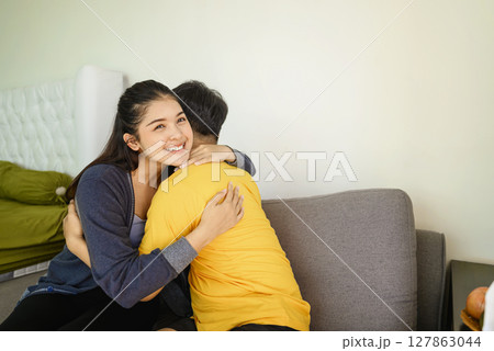 Indonesian southeast asian affectionate couple embracing while sitting on the couch at home Indonesian southeast asian affectionate couple embracing while sitting on the couch at home 127863044
