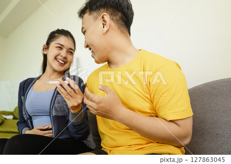 Indonesian southeast asian couple sitting on a sofa at home while looking results of a pregnancy test. Healthcare and family planning concept Indonesian southeast asian couple sitting on a sofa at home while looking results of a pregnancy test. Healthcare and family planning concept 127863045