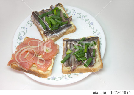 sandwiches with solted fish: sprats and slices of salmon on butter, seasoned with chopped shallots. on white porcelain plate sandwiches with solted fish: sprats and slices of salmon on butter, seasoned with chopped shallots. on white porcelain plate 127864854