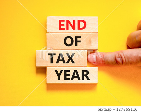 End of tax year symbol. Concept words phrase End of tax year on beautiful wooden blocks. Beautiful yellow paper background. Businessman's hand. Business End of tax year concept. Copy space. End of tax year symbol. Concept words phrase End of tax year on beautiful wooden blocks. Beautiful yellow paper background. Businessman's hand. Business End of tax year concept. Copy space. 127865116