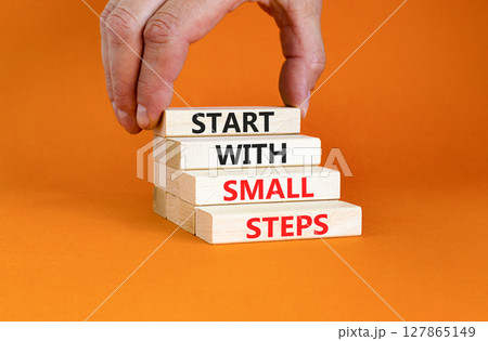 Start with small steps symbol. Concept words phrase Start with small steps on beautiful wooden blocks. Beautiful orange background. Businessman hand Business Start with small steps concept. Copy space 127865149
