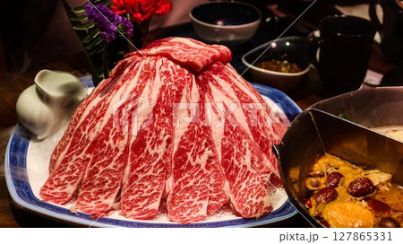 close up of slices of raw uncooked marbled beef in a hill for hot pot. The spicy hot pot on the side close up of slices of raw uncooked marbled beef in a hill for hot pot. The spicy hot pot on the side 127865331