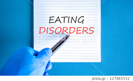 Eating disorders symbol. Concept words Eating disorders on beautiful white note. Doctor's hand in blue medical glove. Beautiful blue background. Medical healthy lifestyle eating disorders concept. 127865552