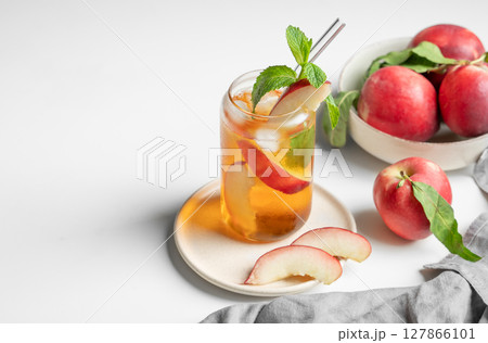 Ice tea with peach, mint in a glass on a white table near window with fresh fruits and sunlight. Ice tea with peach, mint in a glass on a white table near window with fresh fruits and sunlight. 127866101