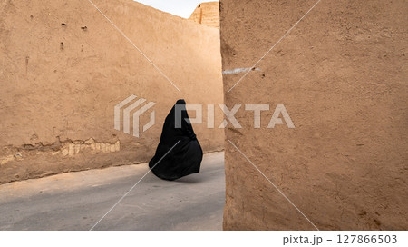 Unidentified muslim woman, dressed in black hijab walks on the narrow street of old city Yazd Unidentified muslim woman, dressed in black hijab walks on the narrow street of old city Yazd 127866503