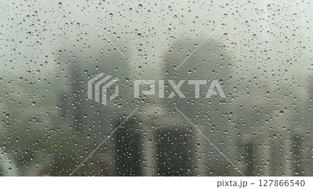 Rainy day view through a window with water droplets clinging to the glass, blurring the urban cityscape outside, creating a serene and introspective mood 127866540