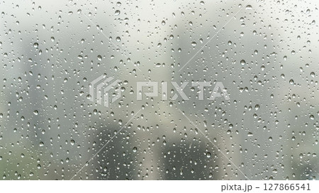 Rainy day view through a window with water droplets clinging to the glass, blurring the urban cityscape outside, creating a serene and introspective mood 127866541