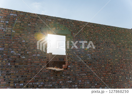 Bright sunlight shines through an unfinished window opening in a newly constructed brick wall on a building site 127868250
