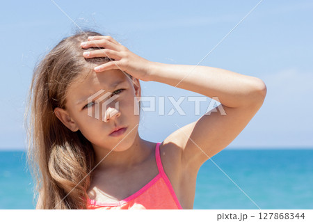 Caucasian child of 8 9 years looking at camera holding hand on forehead showing heatstroke on sea beach Caucasian child of 8 9 years looking at camera holding hand on forehead showing heatstroke on sea beach 127868344