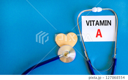 Vitamin A symbol. Concept words Vitamin A on beautiful white card. Wooden heart and stethoscope. Beautiful blue background. Medical healthy lifestyle Vitamin A concept. 127868554