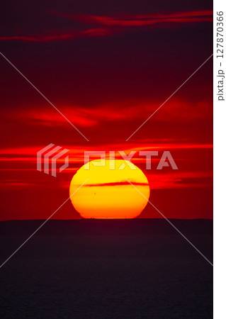 Vibrant sunset over the sea horizon with a dark silhouette of distant hills. 127870366
