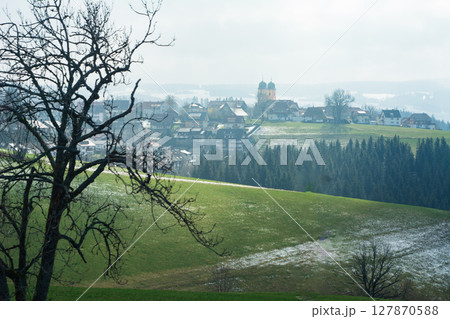 Breathtaking view of a serene village nestled in rolling green hills under a cloudy sky in early springtime, capturing the essence of tranquility and nature's beauty 127870588