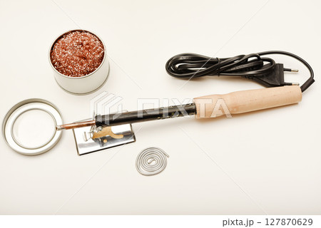 A soldering iron with a wooden handle with solder and a stand. Soldering iron and stinger cleaner. 127870629