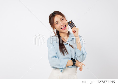 Young asian woman smiling, thinking what to buy, holding credit card and looking at copy space dreaming of a purchase using her bank card, isolated studio white background Young asian woman smiling, thinking what to buy, holding credit card and looking at copy space dreaming of a purchase using her bank card, isolated studio white background 127871145