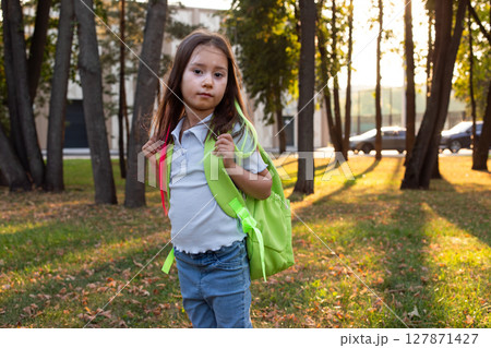 Young girl in park with backpack during golden hour 127871427