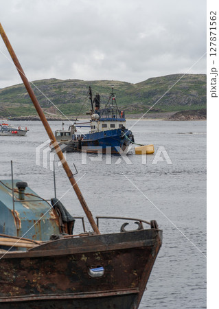 Rusty fishing boats and sunken shipwrecks in the famous ship graveyard of Teriberka under overcast skies 127871562