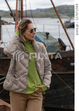 Woman standing near rusty abandoned fishing boats at the ship graveyard in Teriberka 127871569