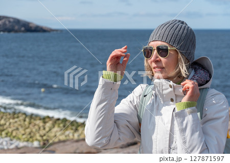Woman standing on the rocky shore of the Barents Sea in Teriberka, Russia, adjusting her sunglasses Woman standing on the rocky shore of the Barents Sea in Teriberka, Russia, adjusting her sunglasses 127871597