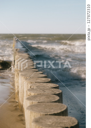 row of logs on beach. pier made of wooden beams on sand. row of logs on beach. pier made of wooden beams on sand. 127872310