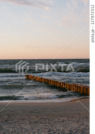 Wooden pier in water on background of ocean. sky is orange, and water is choppy, ocean is agitated. Wooden pier in water on background of ocean. sky is orange, and water is choppy, ocean is agitated. 127872312