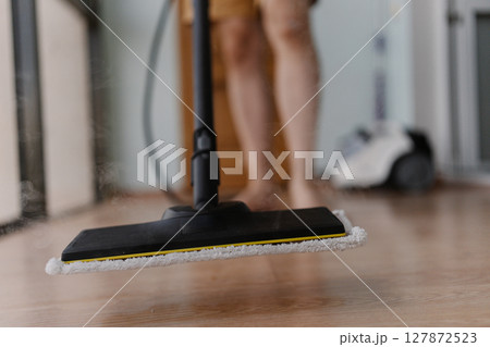Wooden floor receiving deep cleaning through powerful steam mop, generating hot steamy vapor and showcasing thorough household sanitation method, close-up. Concept of housekeeping and cleaning. 127872523