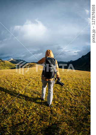 Woman backpacker hiking on high altitude mountains taking picture of the snow capped mountain in the distance Woman backpacker hiking on high altitude mountains taking picture of the snow capped mountain in the distance 127876808